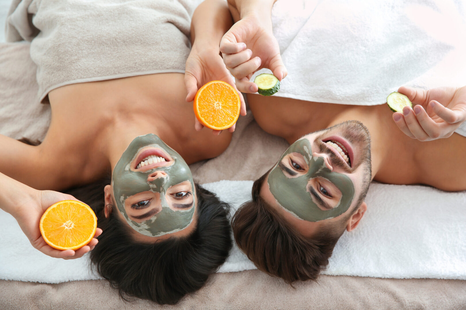 Paar liegend mit Fruchtsäure Maske im Gesicht. Orange und Gurkenscheibe in der Hand